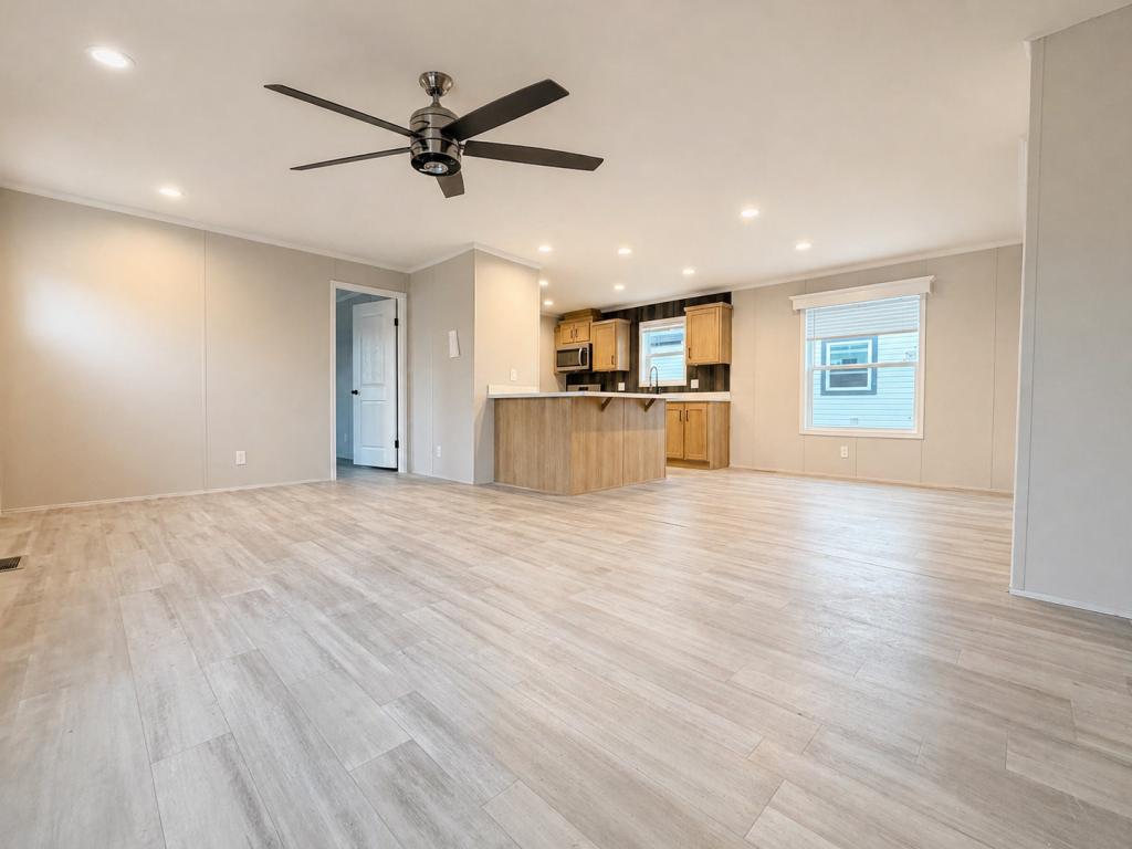 Spacious, modern living area with light wood floors, ceiling fan, and open kitchen with wood cabinets.