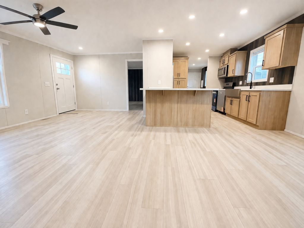Spacious, empty kitchen and living area with light wood floors and modern cabinets.