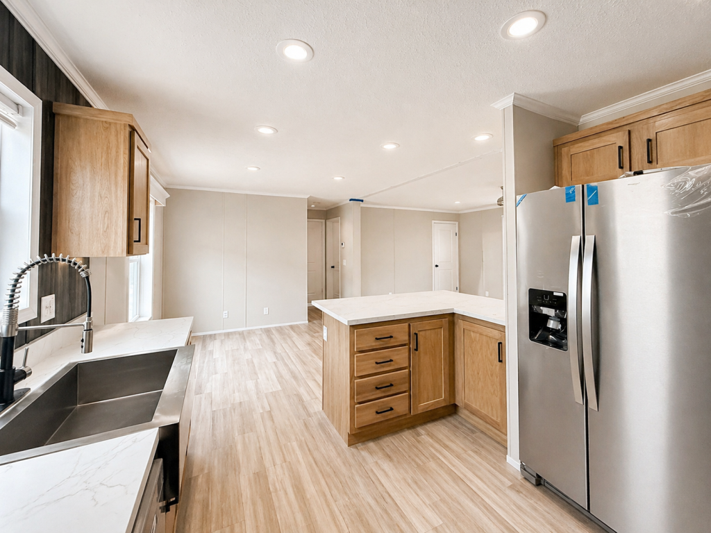 Modern kitchen with light wood cabinets, stainless steel appliances, and marble countertops under bright lighting.