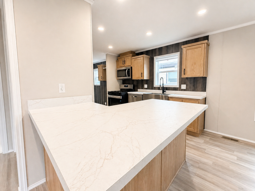 Modern kitchen with light wood cabinets, marble countertops, stainless steel appliances, and recessed lighting.
