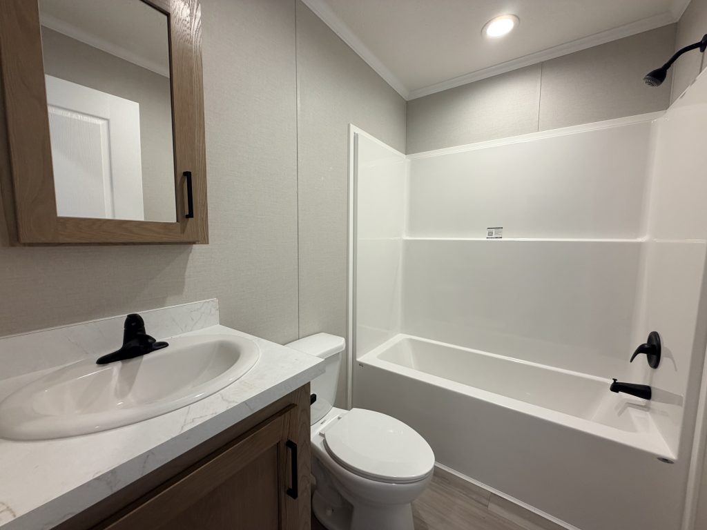 Modern bathroom with a sink, toilet, wooden cabinet, and a white bathtub-shower combo, under bright lighting.