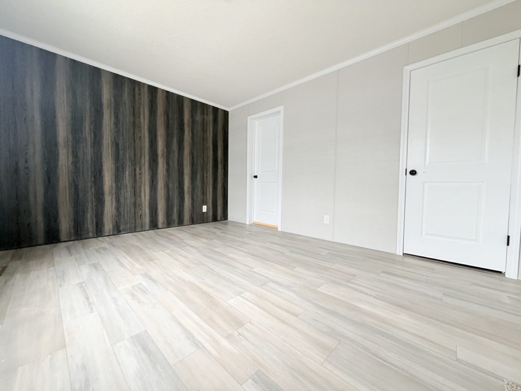 Empty room with wood-patterned floor, white walls, two white doors, and a dark accent wall.