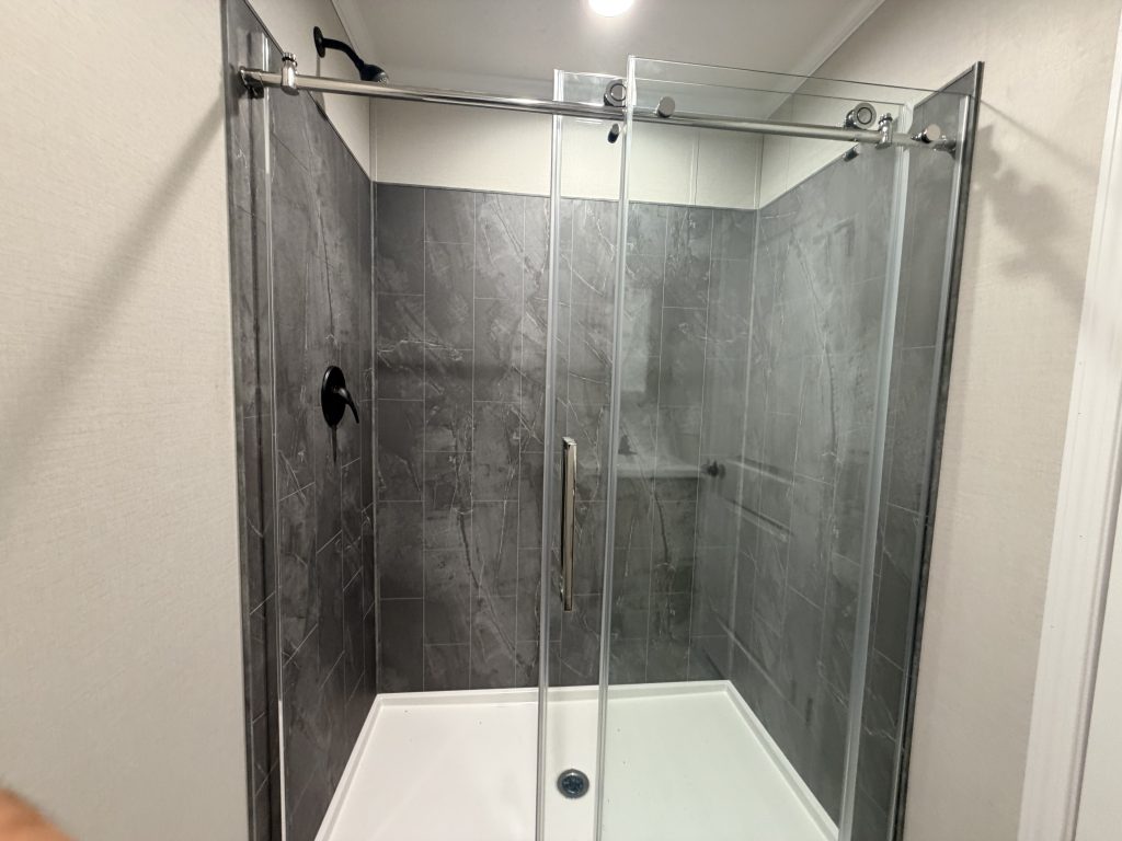 Modern shower with gray tile walls, glass sliding doors, black fixtures, and a white shower base.