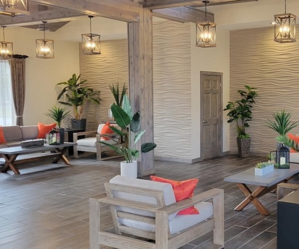 Modern lounge with wooden furniture, gray tile floor, orange cushions, plants, and geometric pendant lights.