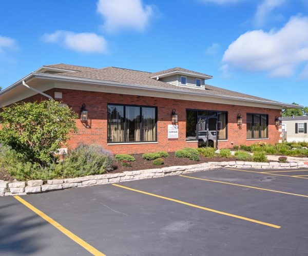 Single-story brick office building with large windows, surrounded by landscaped plants and an empty parking lot.